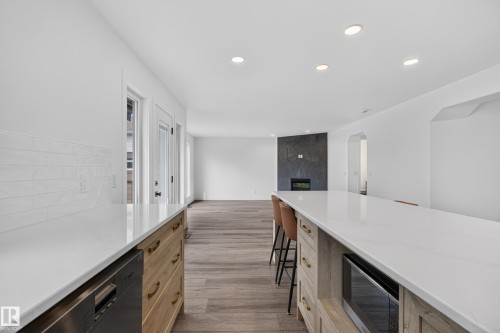 Expansive kitchen island with white countertop, recessed lighting, wood-finish flooring, built-in microwave, and contemporary fireplace feature - 229 Hillcrest Crest, Sherwood Park, AB - Indoor Photo Showing Other Room