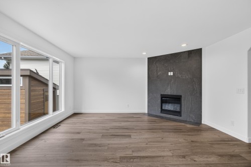 Expansive room featuring wood-finish flooring, large windows, a built-in fireplace with a dark stone-finish surround, and recessed lighting - 229 Hillcrest Crest, Sherwood Park, AB - Indoor With Fireplace