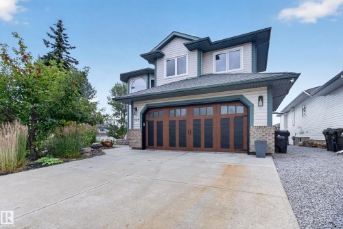 Light-colored siding exterior with dark trim accents, a large concrete driveway, a wood-finish garage door with dark paneling, and an arched window - 229 Hillcrest Crest, Sherwood Park, AB - Outdoor