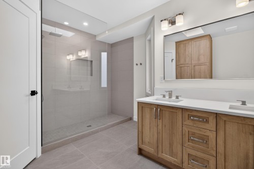 Frameless glass shower enclosure with a recessed shelf, dual-sink vanity with wood-finish cabinetry, white countertop, and brushed nickel hardware - 229 Hillcrest Crest, Sherwood Park, AB - Indoor Photo Showing Bathroom
