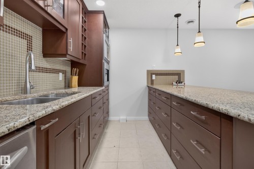 U-shaped kitchen with extensive dark wood cabinetry, light-toned granite countertops, a tile backsplash, and stainless steel appliances - 229 Hillcrest Crest, Sherwood Park, AB - Indoor Photo Showing Kitchen With Double Sink