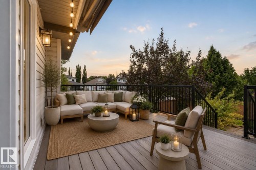Elevated deck featuring composite wood-finish flooring and black metal railings, anchored by a curved sectional seating area with neutral upholstery and a round concrete fire table - 229 Hillcrest Crest, Sherwood Park, AB - Outdoor With Deck Patio Veranda