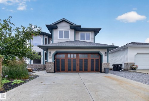Two-story exterior with light gray siding, dark wood-finish garage door, stone accents, and a concrete driveway - 229 Hillcrest Crest, Sherwood Park, AB - Outdoor With Facade