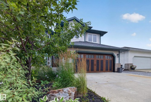 Exterior featuring a wood-finish garage door, white siding, dark trim, concrete driveway, and established landscaping - 229 Hillcrest Crest, Sherwood Park, AB - Outdoor