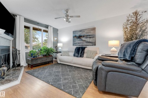 Wood-finish flooring throughout, complemented by a ceiling fan with integrated lighting - 6008 37 Avenue Nw, Edmonton, AB - Indoor Photo Showing Living Room With Fireplace