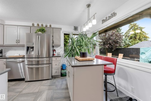 Kitchen featuring grey cabinetry, stainless steel appliances, a center island with countertop seating, and a large window - 6008 37 Avenue Nw, Edmonton, AB - Indoor Photo Showing Kitchen