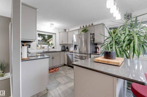 Kitchen featuring gray cabinetry, stainless steel appliances, tile flooring, a window, and a peninsula with a dark countertop - 6008 37 Avenue Nw, Edmonton, AB - Indoor Photo Showing Kitchen