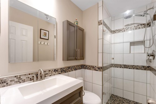 Vanity with an integrated sink and brushed nickel faucet, wall-mounted medicine cabinet with integrated lighting, glass-enclosed shower with mosaic tile accents, and a built-in shower niche - 6008 37 Avenue Nw, Edmonton, AB - Indoor Photo Showing Bathroom