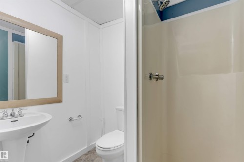 Pedestal sink with chrome-finish faucet, framed mirror, and a stand-up shower with chrome-finish fixtures - 6008 37 Avenue Nw, Edmonton, AB - Indoor Photo Showing Bathroom