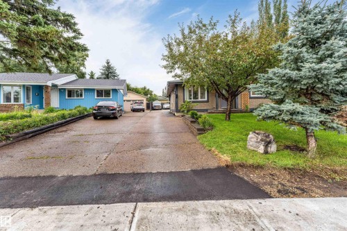 Manicured front lawn with mature trees, paved driveway, and established garden beds - 6008 37 Avenue Nw, Edmonton, AB - Outdoor