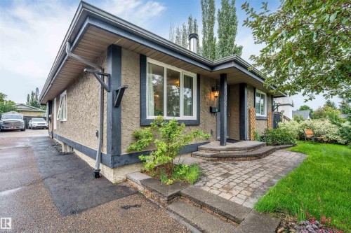 Stucco exterior with dark trim, featuring a paved driveway, stone paver walkway, and a landscaped front yard with mature greenery - 6008 37 Avenue Nw, Edmonton, AB - Outdoor