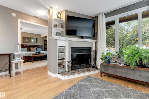 Wood-finish flooring, built-in fireplace with a stone surround, built-in shelving, and expansive windows - 6008 37 Avenue Nw, Edmonton, AB - Indoor Photo Showing Living Room With Fireplace