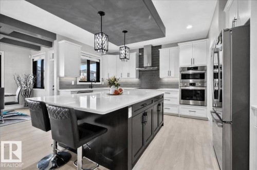 Expansive kitchen island with a white countertop, two pendant lights, stainless steel appliances, and white cabinetry - 6813 Knox Loop Sw, Edmonton, AB - Indoor Photo Showing Kitchen With Upgraded Kitchen