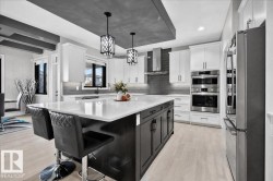Expansive kitchen island with a white countertop, two pendant lights, stainless steel appliances, and white cabinetry - 