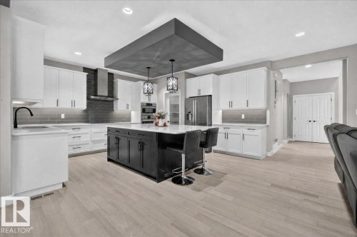 Gourmet kitchen featuring a large central island with pendant lighting, stainless steel appliances, extensive white cabinetry, and light wood-finish flooring - 6813 Knox Loop Sw, Edmonton, AB - Indoor Photo Showing Kitchen With Upgraded Kitchen