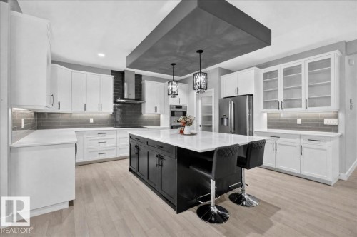 Modern kitchen featuring a central island with seating, stainless steel appliances, white cabinetry, wood-finish flooring, and a dark subway tile backsplash - 6813 Knox Loop Sw, Edmonton, AB - Indoor Photo Showing Kitchen With Upgraded Kitchen