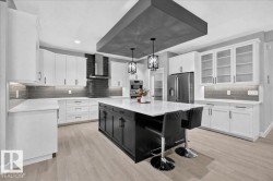 Modern kitchen featuring a central island with seating, stainless steel appliances, white cabinetry, wood-finish flooring, and a dark subway tile backsplash - 