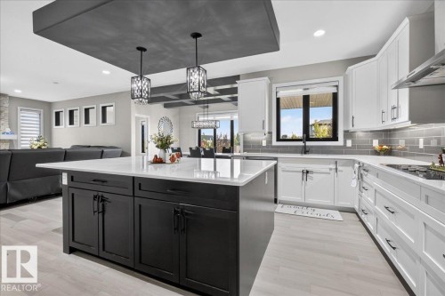 Kitchen featuring a central island with dark cabinetry, white countertops, subway tile backsplash, and light wood-finish flooring - 6813 Knox Loop Sw, Edmonton, AB - Indoor Photo Showing Kitchen With Upgraded Kitchen