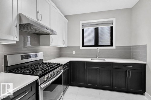 Two-tone cabinetry with white upper and dark lower units, stainless steel range with overhead vent, gray subway tile backsplash, and light countertops - 6813 Knox Loop Sw, Edmonton, AB - Indoor Photo Showing Kitchen With Upgraded Kitchen