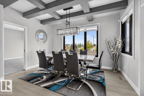 Modern dining space featuring a coffered ceiling with recessed lighting, a geometric pendant fixture, and expansive windows framing natural light and outdoor scenery - 6813 Knox Loop Sw, Edmonton, AB - Indoor Photo Showing Dining Room