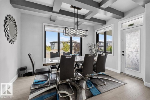 Coffered ceiling with a linear chandelier, large windows with roller blinds, wood-finish flooring, and a decorative glass entry door - 6813 Knox Loop Sw, Edmonton, AB - Indoor
