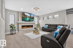 Light wood-finish flooring, stone-clad fireplace with mantel, recessed electric fireplace, multiple windows with blinds, and a decorative ceiling fixture - 
