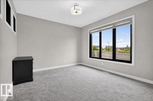 Neutral wall paint, ceiling-mounted light fixture, large picture window with black framing, white window trim, and grey carpeting - 6813 Knox Loop Sw, Edmonton, AB - Indoor Photo Showing Other Room