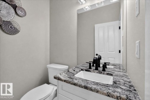 Vanity with a speckled countertop and integrated sink, matte black fixtures, and a wall-mounted mirror with overhead lighting - 6813 Knox Loop Sw, Edmonton, AB - Indoor Photo Showing Bathroom
