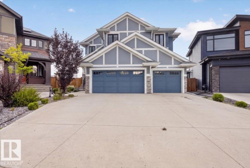 Gable-roof exterior with blue siding and white trim, featuring two attached garage bays with blue doors, stone accents, and a concrete driveway - 6813 Knox Loop Sw, Edmonton, AB - Outdoor With Facade