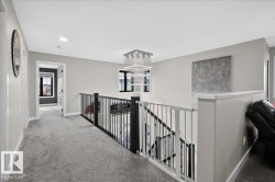 Plush carpeted flooring, metal baluster railing, and a multi-tiered chandelier - 