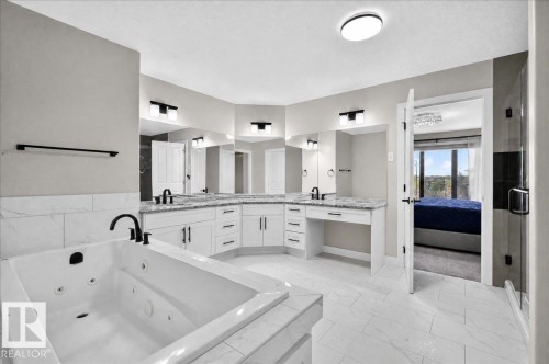 Jetted soaking tub, dual vanity sinks, white cabinetry, dark-finish fixtures, and tiled flooring - 6813 Knox Loop Sw, Edmonton, AB - Indoor