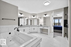 Jetted soaking tub, dual vanity sinks, white cabinetry, dark-finish fixtures, and tiled flooring - 