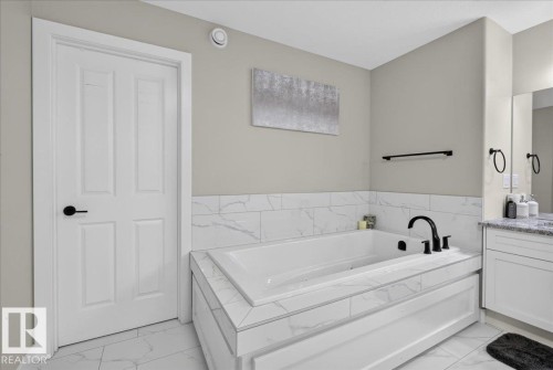 Recessed soaking tub with dark-finish fixtures, white paneled surround, and tile backsplash - 6813 Knox Loop Sw, Edmonton, AB - Indoor Photo Showing Bathroom