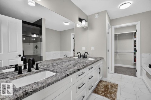 Dual vanity with undermount sinks and black fixtures, granite countertop, white cabinetry with black hardware, glass-enclosed shower, and built-in closet shelving - 6813 Knox Loop Sw, Edmonton, AB - Indoor Photo Showing Bathroom