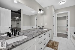 Dual vanity with undermount sinks and black fixtures, granite countertop, white cabinetry with black hardware, glass-enclosed shower, and built-in closet shelving - 