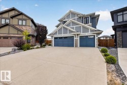 Modern exterior with gray siding, stone accents, two attached garages with blue doors, and a concrete driveway - 