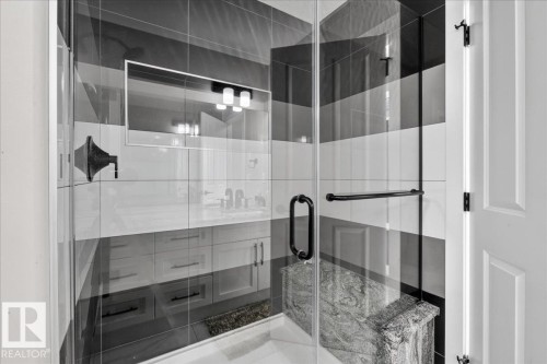 Glass-enclosed shower with horizontal striped tiling, a built-in stone bench, and matte black hardware - 6813 Knox Loop Sw, Edmonton, AB - Indoor Photo Showing Bathroom