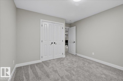 Neutral wall tones with white trim, gray patterned carpeting, and white bifold doors - 6813 Knox Loop Sw, Edmonton, AB - Indoor Photo Showing Other Room