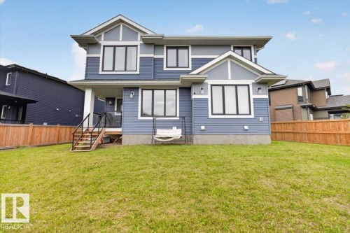 Expansive backyard featuring a manicured lawn, wood fencing, and a covered patio with a staircase - 6813 Knox Loop Sw, Edmonton, AB - Outdoor