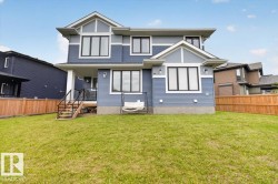 Expansive backyard featuring a manicured lawn, wood fencing, and a covered patio with a staircase - 