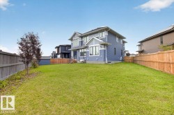 Expansive rear yard with a manicured lawn, full privacy fencing, and exterior lighting fixtures - 