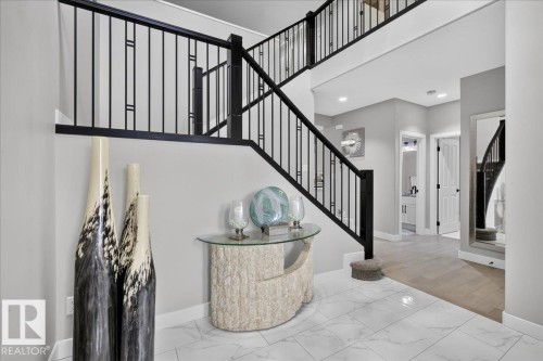 Two-story entryway featuring a black wrought iron staircase and white marble-look tile flooring - 6813 Knox Loop Sw, Edmonton, AB - Indoor Photo Showing Other Room