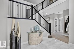 Two-story entryway featuring a black wrought iron staircase and white marble-look tile flooring - 