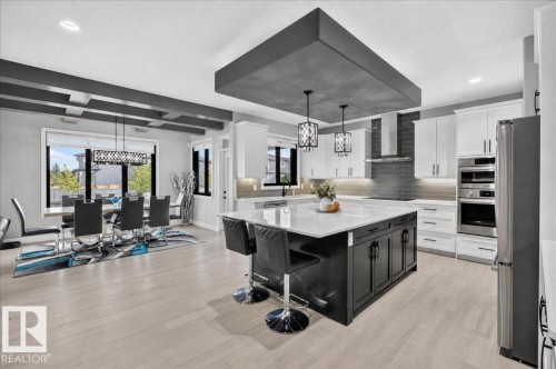 Spacious open-concept kitchen and dining area featuring light wood-finish flooring, a large kitchen island with a light-toned countertop, white cabinetry, integrated stainless steel appliances, and a modern dining light fixture - 6813 Knox Loop Sw, Edmonton, AB - Indoor
