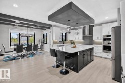 Spacious open-concept kitchen and dining area featuring light wood-finish flooring, a large kitchen island with a light-toned countertop, white cabinetry, integrated stainless steel appliances, and a modern dining light fixture - 