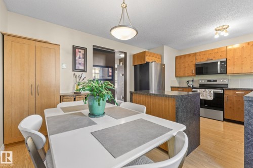 Kitchen and dining area featuring wood-finish flooring, two-tone cabinetry, stainless steel appliances, and a central island with a stone-finish countertop - 17132 103 Street Nw, Edmonton, AB 