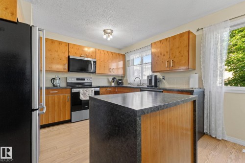 Wood-finish flooring with a central island featuring a dark countertop - 17132 103 Street Nw, Edmonton, AB 