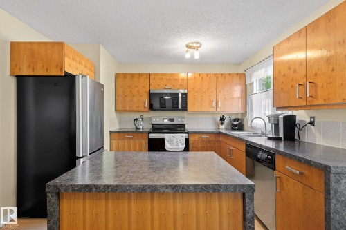 Kitchen featuring a central island with a stone-finish countertop, wood-finish cabinetry, stainless steel appliances, and a tile backsplash - 17132 103 Street Nw, Edmonton, AB 
