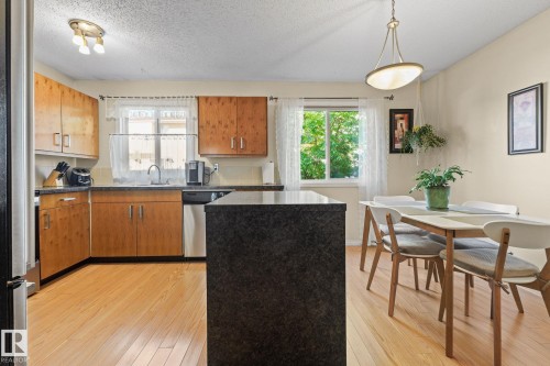 Kitchen and dining area featuring wood-finish flooring, built-in wooden cabinetry, dark countertops, and a central island - 17132 103 Street Nw, Edmonton, AB 