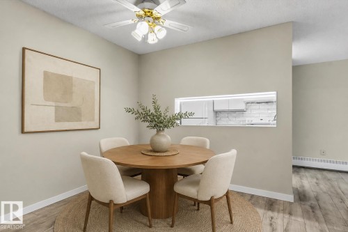 Open concept dining area featuring a pass-through window, wood-finish flooring, and a ceiling fan - #102 6710 158 Av Nw, Edmonton, AB 